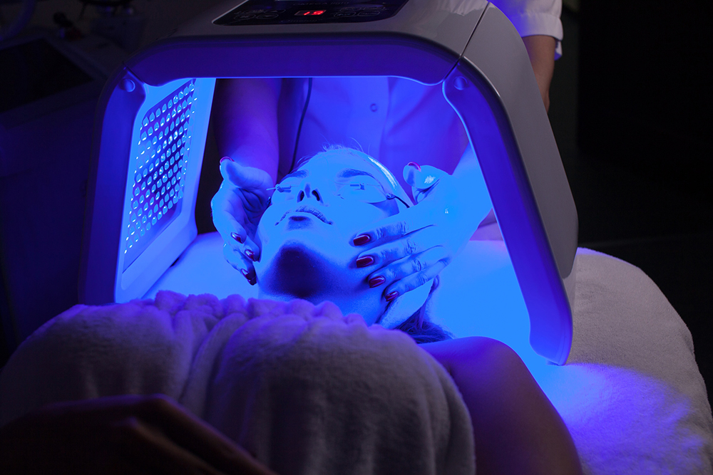 Young woman having LED light facial treatment in beauty salon